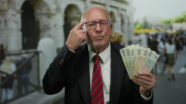 Takım elbiseli son sınıf öğrencisi elinde Czech Koruna banknotları Roma Kolezyum Caddesi 'nin yakınındaki açık havada el kol hareketleri yapıyor..