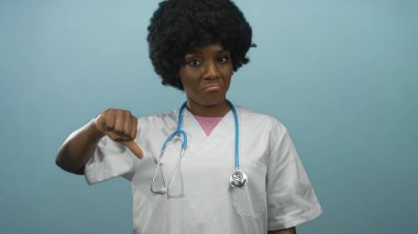 Steteskoplu beyaz önlüklü kadın doktor mavi stüdyoda baş parmağını kaldırıyor..