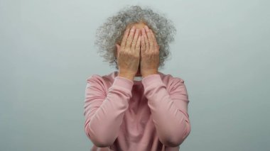 Beyaz tenli arka planda gülümseyen ve yüzünü gösteren gri saçlı yaşlı bir kadın..