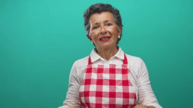 Gri saçlı, kırmızı kareli önlüklü yaşlı kadın canlı yeşil bir arka planda uyuyor, dinleniyor ve rahatlıyor..