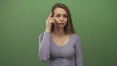 Yeşil bir zemin üzerinde odaklanmış ifade ile düşünen ve kameraya işaret eden kadın, tecrit edilmiş bir ortamda tefekkür, odaklanma ve iletişim iletiyor..
