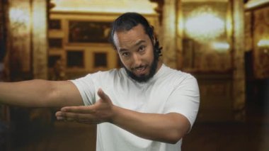 Kolları açık bir adam, beyaz tişört ve sakal giyen, süslemeli bir kilisenin içinde avuçlarını ileri doğru uzatıyordu..