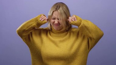 Mor arka plan karşısında kulaklarını tıkayan bir kadın hardal süveter giyiyor ve ciddi bir ifadeyle rahatsız edici bir ses çıkarıyor..