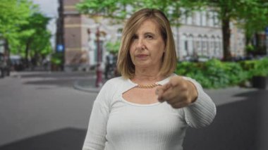 Beyaz kazak giyen kadın, tarihi binanın önündeki caddede kameraya işaret ediyor; kararlılık.