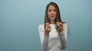 Elleri ve parmakları olan bir kadın, mavi stüdyoda kameraya doğru beyaz bir bluz giyiyor, yüzünde canlandırılmış yüz ifadesi olan genç bir yetişkin;.