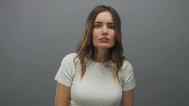 Hafifçe aydınlatılmış hafif gri stüdyo ortamında kameraya bakan kadın yüzü; sessiz tefekkür.