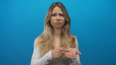 Avuçları açık, mavi stüdyoda para isteyen sarışın beyaz bir kadın. Çaresizlik için merhamet gerekir..