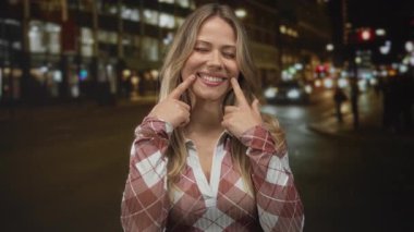 Sarışın kadın gülümseyen ağız, meşgul bir şehir caddesinde her iki işaret parmağını işaret ediyor; neşe ve neşe.