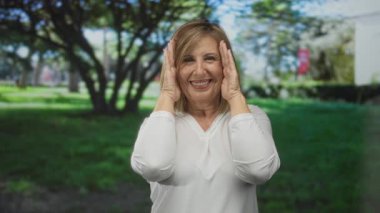 Güneşli bir öğleden sonra yeşil şehir parkında elleri olan ve geniş bir gülümseme içinde gülümseyen kadın:.