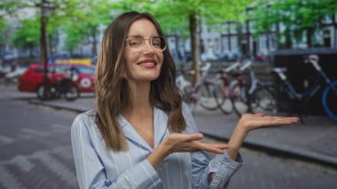 Gözlüklü kadın ellerini yana uzatıyor ve şehir caddesinde baş parmak kaldırıyor. Güven onayı..