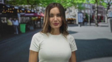 Beyaz tişörtlü, çıplak elleriyle şehir caddesinde el hareketi yapan genç bir kadın..