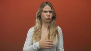 Stüdyoda eli, parmağı ve dudağı kaplayan kadın, turuncu arka planda jest yapıyor. Sürpriz şok..