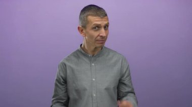 Kısa saçlı, gri tişörtlü, elleri mor bir duvara dayanmış, duygularını izole bir şekilde ifade eden bir adam..