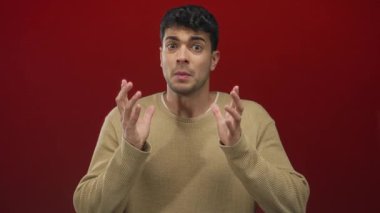 Erkekler, arka plan kırmızısı ve endişeli ifade ile genç İspanyol erkeğin stüdyo portresinde el kaldırır..