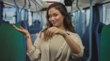 Gülümseyen genç kadın, otobüsün içinde sağ elinde yeşil koltuklar ve üstten raylar olan bir tabela tutuyor..