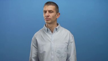 Çizgili tişörtlü adam mavi arka plana karşı duruyor. Ciddi bir ifadeyle yana bakıyor. Tarafsız bir ayarı vurguluyor..