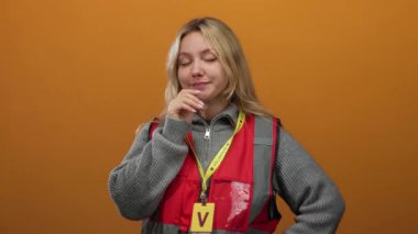 İzole edilmiş turuncu arka planda kırmızı yelek giyen genç gönüllü kadın düşünceli görünüyor..