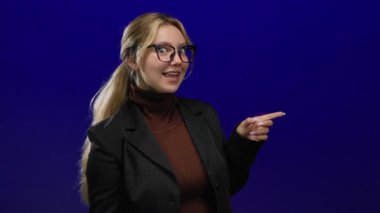 Gülümseyen ve iş kıyafetlerini gösteren bir kadın canlı mavi arka planda, kendine güvenen bir poz sergiliyor..