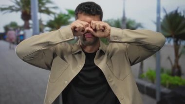 Tahta kaldırımda gözlerini ovuşturan genç İspanyol adam, inançsızlık şoku..