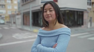 Mavi kazaklı genç Çinli kadın, sakin bir şehir caddesinde kollarını kavuşturarak, şehir hayatının özünü yakalıyor..