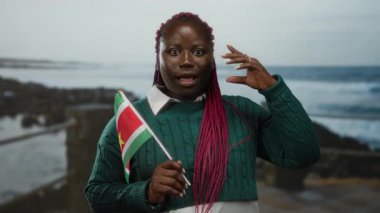 Woman with suriname flag gesturing idea on beach with sea background, depicting outdoor setting and cultural pride.