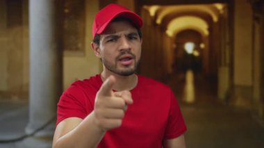 Kırmızı şapkalı ve kırmızı gömlekli genç İspanyol kurye eski üniversite binası koridorunu işaret ediyor..