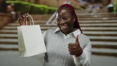 Alışveriş torbası tutan ve şehir merdivenlerinde baş parmağını sallayan bir kadın..