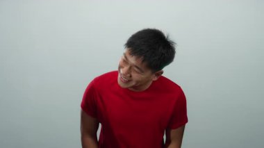 Kırmızı tişört giyen genç Çinli adam neşeli bir şekilde izole edilmiş beyaz arka plana gülümsüyor, neşeli ifadelerde pozitif duygular ve mutluluk gösteriyor..