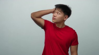 Kırmızı gömlekli genç adam, beyaz arka plan duvarına karşı çeşitli düşünceli ifadeler sergiliyor..