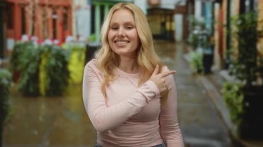 Canlı bir şehir sahnesinde, açık havada pembe gömlekli, sarı saçlı, renkli bir şehir caddesini gösteren bir kadın..