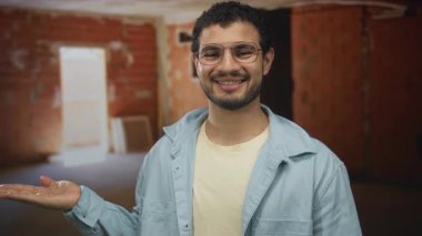 Gözlüklü genç İspanyol adam gülümsüyor ve inşaat halindeki avuç içini gösteriyor. İyimserlik..