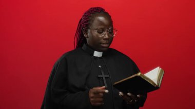 İzole edilmiş kırmızı arka plan duvarına karşı İncil okuyan kadın rahip ruhaniliği, liderliği ve inancı ciddi bir ifade ve odaklanmış tavırla somutlaştırıyor..