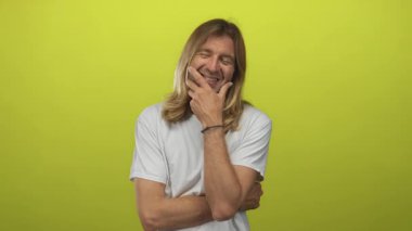 Sarışın, uzun saçlı, eli çenesinde gülümseyen ve kolları çaprazlanmış bir adam, yeşil ışık altında stüdyoda; yansıma.