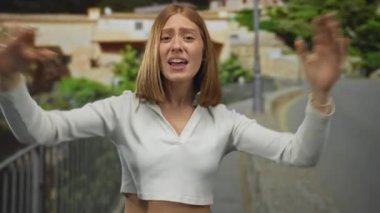 Beyaz tarladaki genç sarışın kadın çıplak kollarıyla kaldırım taşı caddesine işaret ediyor; acil savunma hüsranı.