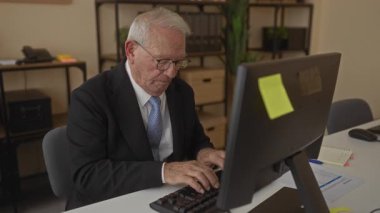 Ofisteki bir bilgisayarda çalışan takım elbiseli kıdemli bir adam profesyonel bir iş ortamını gösteriyor..