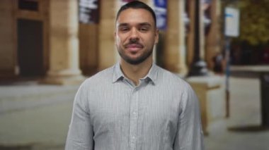 Gülümseyen ve barış işareti yapan genç adam, süslü binanın önündeki canlı güneşli caddede barış yapıyor..