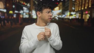 Beyaz kazaklı genç adam gece hareketli şehir caddesinde sessiz kalmak için dudak dudağa geziyor..