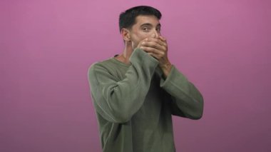 Yeşil kazaklı genç adam mor stüdyoda elleri ile ağzını kapatır..