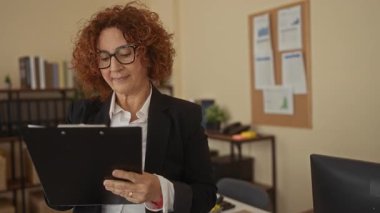 Modern ofiste dokümanlar, raflar, çizelgeler ve profesyonel çevre ile çevrili panoyu inceleyen kadın, iş ve organizasyonu sergiliyor.