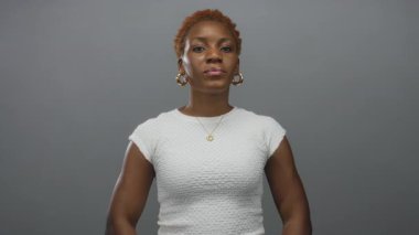 Kadın, kamerayla göz teması kurarken gri bir stüdyoda dua jestinde el ele tutuşuyor; inanç umudu..