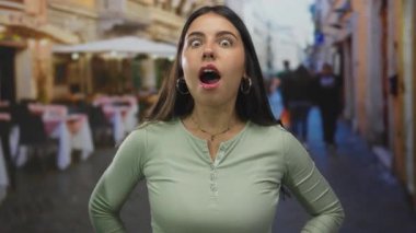 İfadesi olan bir kadın gün boyunca arka planda teras restoranı ile caddede duruyor, canlı bir şehir atmosferini yakalıyor..