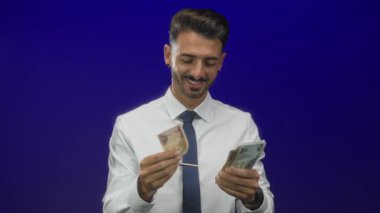 Kıtır kıtır beyaz gömlekli ve kravatlı gülümseyen adam stüdyo ortamında iki eliyle uae dirham banknotları sayıyor; refah.