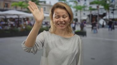 Gri bluzlu kadın gülümseyen ve sokakta el sallayan bulanık kalabalık ve arkasında bina; bağlantı sevinç karşılama.