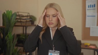 Ofisteki kadın, çalışma ortamının zorlu olduğunu belirten çizelgeler ve bitkilerle çevrili baskı ve yorgunluk hissediyor..