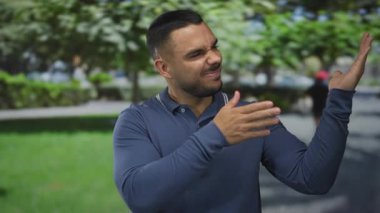 Genç İspanyol adam geniş bir gülümseme ve yeşil ağaçların altında sokak parkında sol parmağını işaret ederek; coşku.