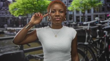 Nehir kenarındaki işlek kanal caddesinde parmağı işaret eden kadın ve park edilmiş bisikletler; iç tefekkür.