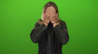 Yeşil bir stüdyo arka planına karşı elleri ile yüzünü kapatan bir adam geniş bir gülümseme ve onun uzun sarı saç geri çekin; sürpriz eğlence.