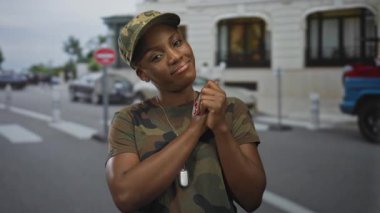 Kamuflaj üniformalı kadın, tarihi binanın yakınındaki sokakta askeri bir şapka takarken el ve künye takıyor..