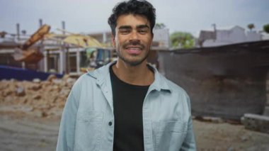 Adam gün ışığında gülümserken kısmen inşa edilmiş bir binanın yanındaki kazıcıyı işaret ediyor; güven belirleme motivasyon artışı.