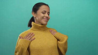 Yeşil bir arka planda, hardal süveter giymiş bir kadın izole edilmiş, genç, İspanyol cazibesi ve günlük tarzıyla kendine güveni ve sıcaklığı yayıyor..